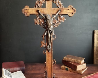 May include: A wooden crucifix with a carved ivy design and a bronze Jesus figure. The crucifix is on a wooden base.