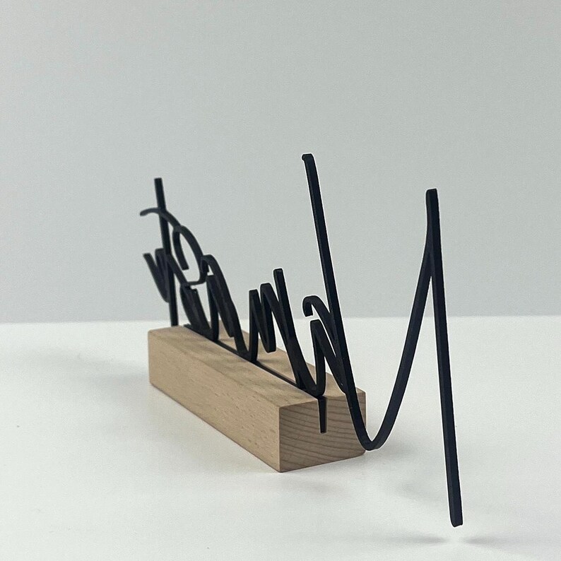 May include: A black metal word art piece that reads "Brand" in a cursive font, mounted on a rectangular wooden base. The word art is a decorative item.