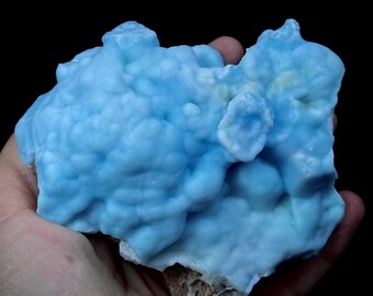 Op de afbeelding: Een groot, blauw, mineraal specimen met een bubbelig, getextureerd oppervlak. Het mineraal is lichtblauw van kleur en heeft een ruwe, ongelijke textuur.