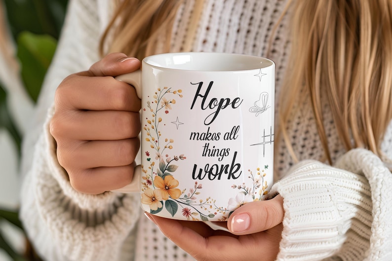 May include: White ceramic mug with the words "Hope makes all things work" in black script. The mug features floral and butterfly illustrations in soft colors. A star and a hashtag-like symbol are also present.