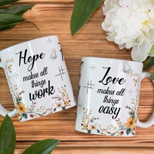 May include: Two white ceramic mugs with floral designs and inspirational quotes. One mug reads "Hope makes all things work," and the other says "Love makes all things easy." The mugs are decorated with butterflies and flowers.