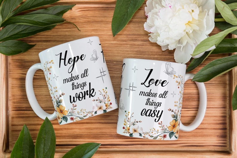 May include: Two white ceramic mugs with floral designs and inspirational quotes. One mug reads "Hope makes all things work," and the other says "Love makes all things easy." The mugs are decorated with butterflies and flowers.