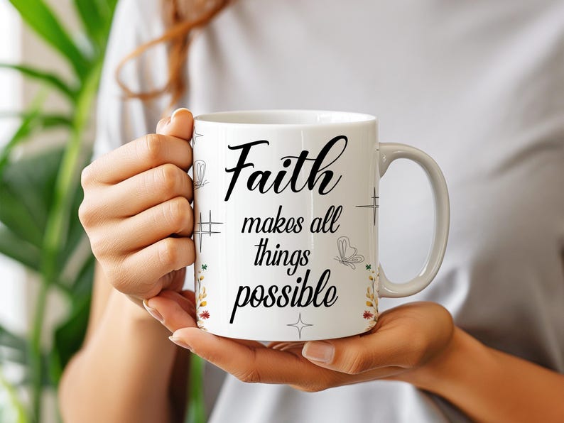 May include: White ceramic mug with the words "Faith makes all things possible" in black script. The mug has a handle and is decorated with small floral and butterfly designs. The mug is held by a person.