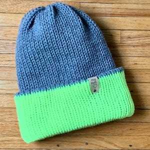 May include: Gray and neon green knit beanie with a small brown tag that says "Hug & Hats" with a heart symbol.