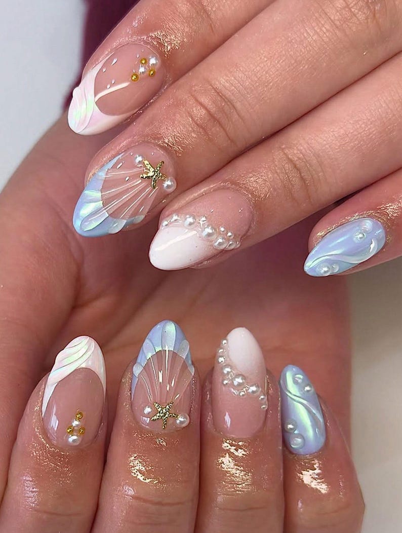 May include: A set of manicured nails with a mermaid theme. The nails feature a variety of designs, including iridescent shell shapes, pearl accents, and gold starfish embellishments. The color palette includes white, light blue, and nude tones.