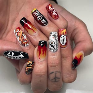 May include: A set of long, oval-shaped acrylic nails with various designs. The nails feature flames, Japanese text, and graphic illustrations in red, yellow, black, and white. The designs include flames, Japanese characters, and a tiger's face.