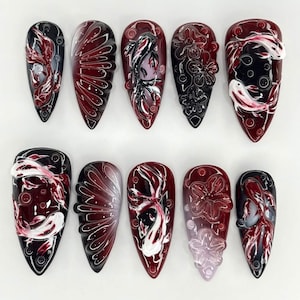 Könnte beinhalten: Ein Set aus zehn künstlichen Nägeln mit aufwendigen Designs. Jeder Nagel hat ein glänzendes Finish mit einer Basis aus Schwarz, Burgunderrot und Weiß. Die Designs umfassen Kois, Blumenmuster und abstrakte Kunst.