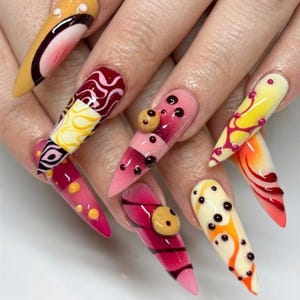 May include: Long, pointed stiletto-shaped artificial nails featuring a vibrant mix of yellow, pink, red, and cream colors. The designs include intricate swirling patterns, raised three-dimensional circular accents, and small dark dots.