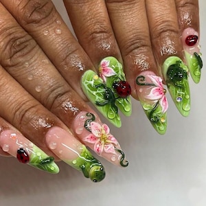 May include: Long, pointed acrylic nails with a nature-themed design. The nails are painted light green with detailed leaves, pink flowers, and red ladybirds. Water droplets are added for a realistic effect to the manicure.