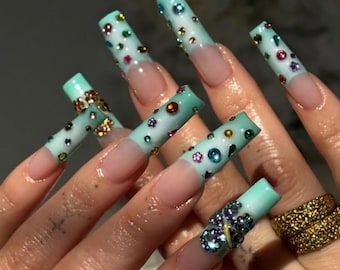May include: Long square-shaped artificial nails featuring a French manicure style with a light mint green tip. The mint green sections are decorated with various small, colorful rhinestones and gems. One nail features a cluster of blue crystals.