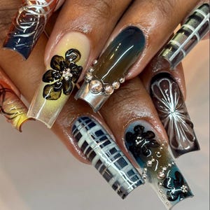 Peut inclure: Ensemble de longs ongles en acrylique carrés avec divers motifs. Certains ongles présentent des motifs floraux avec des strass, tandis que d'autres ont des couleurs dégradées, des motifs à carreaux et des motifs abstraits. La palette de couleurs comprend des nuances de marron, de bleu et de jaune.