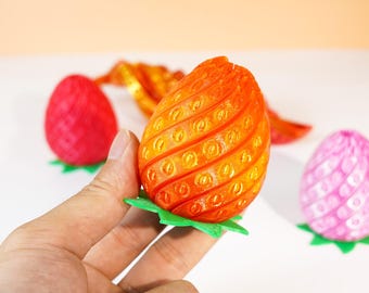 Könnte beinhalten: Ein orangefarbenes, eiförmiges Objekt mit einer texturierten Oberfläche mit Spiralmuster und einer grünen, sternförmigen Basis. Das Objekt weist kleine, kreisförmige Vertiefungen auf der Außenseite auf, die an eine stilisierte Frucht oder einen Dekorationsartikel erinnern.