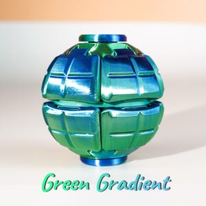 K&ouml;nnte beinhalten: Ein kugelf&ouml;rmiges Fidget-Spielzeug mit metallischem Glanz, das zwischen Gr&uuml;n- und Blaut&ouml;nen wechselt. Das Objekt hat eine segmentierte, gitterartige Oberfl&auml;che mit einem horizontalen Spalt in der Mitte. Darunter steht der Text Green Gradient.