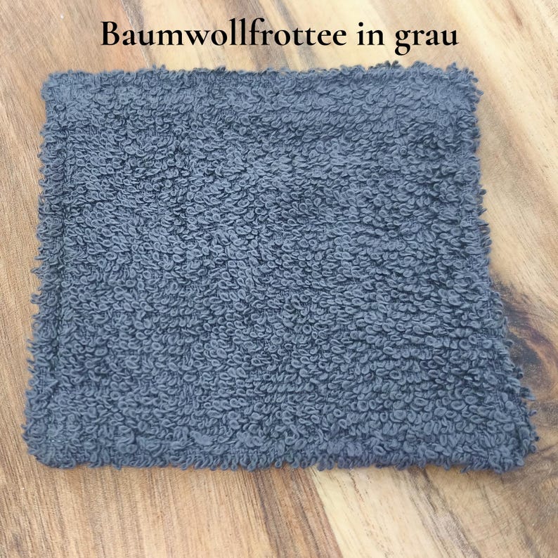 Wiederverwendbare Abschminkpads aus Baumwolle. Obere Seite glatte Baumwolle mit Noten Muster und Rückseite mit Frottee in grau. Ein einzelnes liegt auf einem Holzbrett, in Nahaufnahme zur besseren Ansicht der Rückseite.