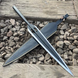 May include: A black and silver sword with a double-edged blade and a long, slender handle. The sword is displayed with its black leather sheath, which has decorative stitching. The blade has two cut-out sections near the handle.