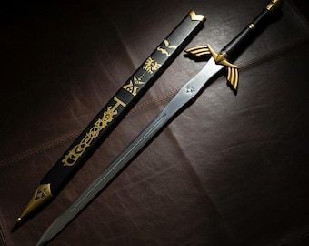 May include: A silver sword with gold accents and a black handle, resting beside its black sheath. The sheath features gold decorative patterns and text. The sword's hilt has gold wings. The blade has a triangular symbol.