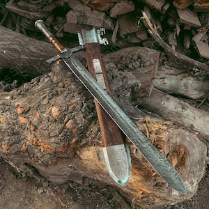 A detailed image Knight Templar Sword with a wooden handle and a silver blade, resting on a pile of logs. The sword's sheath is also visible, made of wood and metal. The overall aesthetic is rustic and historical.