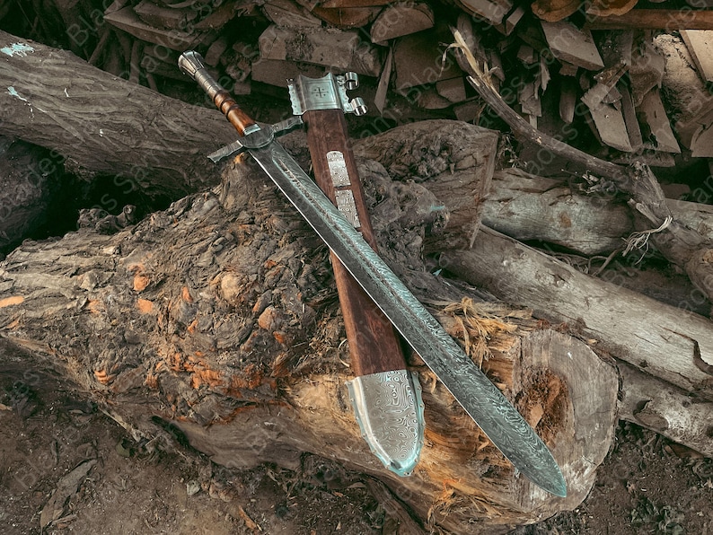 A detailed image Knight Templar Sword with a wooden handle and a silver blade, resting on a pile of logs. The sword's sheath is also visible, made of wood and metal. The overall aesthetic is rustic and historical.