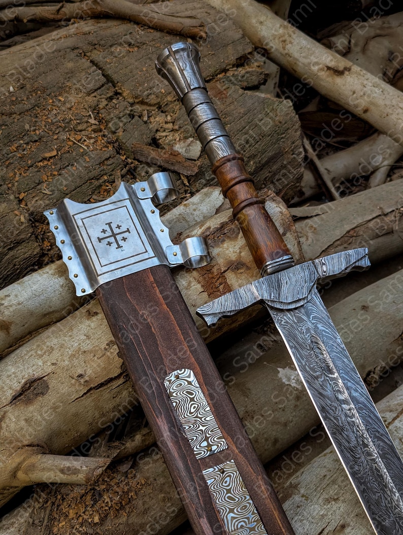 Close up view of the top handle of a hand forged Damascus steel Knight Templar Sword, showing polished hardwood grip, steel fittings, part of the patterned blade, and the upper section of the matching scabbard