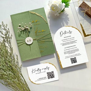 May include: A set of wedding stationery featuring a green invitation with gold lettering and a floral accent. Additional cards include details and a reply card, all with gold trim and QR codes. The invitation reads "Kin Russell".