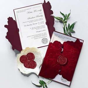May include: Burgundy wedding invitation suite with a floral design, featuring the names Kerta Fioraly and Sandson Ruedig, and wedding details. Includes a seashell dish with red wax seals. The invitation reads "Join us to celebrate our wedding."
