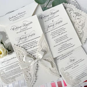 Peut inclure: Faire-part de mariage blancs avec des détails de dentelle découpée au laser. L'ensemble comprend des cartons de réponse, des informations sur l'hébergement et des enveloppes. Un ruban de satin orne l'invitation principale, ajoutant une touche de sophistication. Le texte comprend les noms, les dates et les lieux.