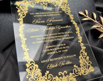 Pode incluir: Convite de casamento em acrílico transparente com letras douradas e borda floral decorativa. O convite inclui os nomes de Travis Freeman e Kaler Graham-Crowther, juntamente com a data, hora e local da cerimónia.