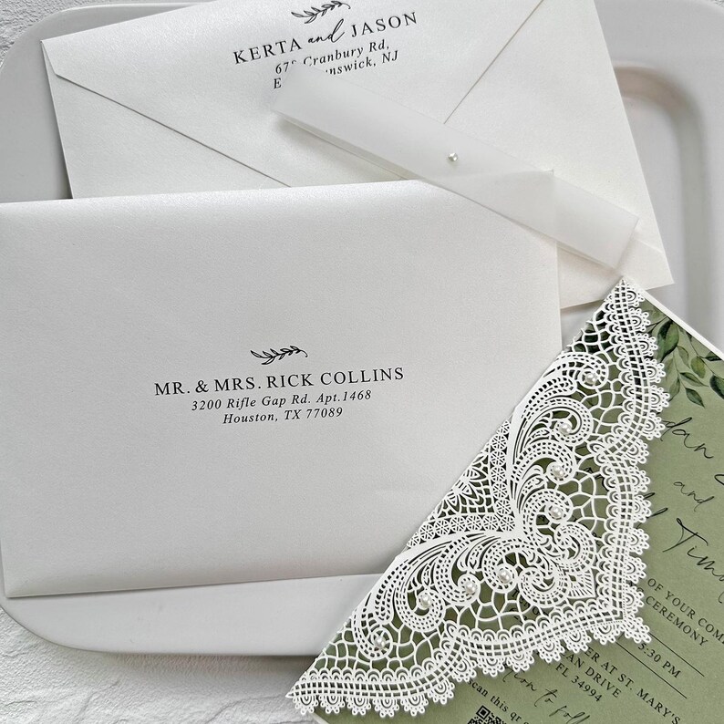 Peut inclure: Un ensemble de faire-part de mariage blanc &eacute;l&eacute;gant, comprenant des enveloppes avec des noms et adresses imprim&eacute;s, et un coin d'invitation d&eacute;coratif d&eacute;coup&eacute; au laser. L'ensemble comprend un ruban et une perle. Le texte comprend des noms, adresses et d&eacute;tails de l'&eacute;v&eacute;nement.