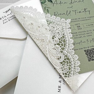 Peut inclure: Invitation de mariage blanche d&eacute;coup&eacute;e au laser avec des d&eacute;tails de dentelle complexes et des accents de perles. L'invitation pr&eacute;sente un fond vert avec les d&eacute;tails de l'&eacute;v&eacute;nement, y compris les noms, la date et l'heure. L'invitation est plac&eacute;e sur une enveloppe blanche.