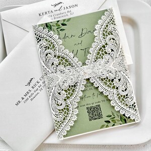 Peut inclure: Un ensemble de faire-part de mariage avec un motif de dentelle blanche d&eacute;coup&eacute;e au laser. La carte d'invitation a un fond vert avec des accents floraux et comprend les noms "Aidan Day and Addie T." et un code QR. Des enveloppes blanches sont &eacute;galement visibles.