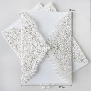 May include: White laser-cut wedding invitations with detailed floral lace patterns. The invitations measure 18.5cm high and 12.8cm wide. The paper has a textured finish, suitable for sophisticated occasions.