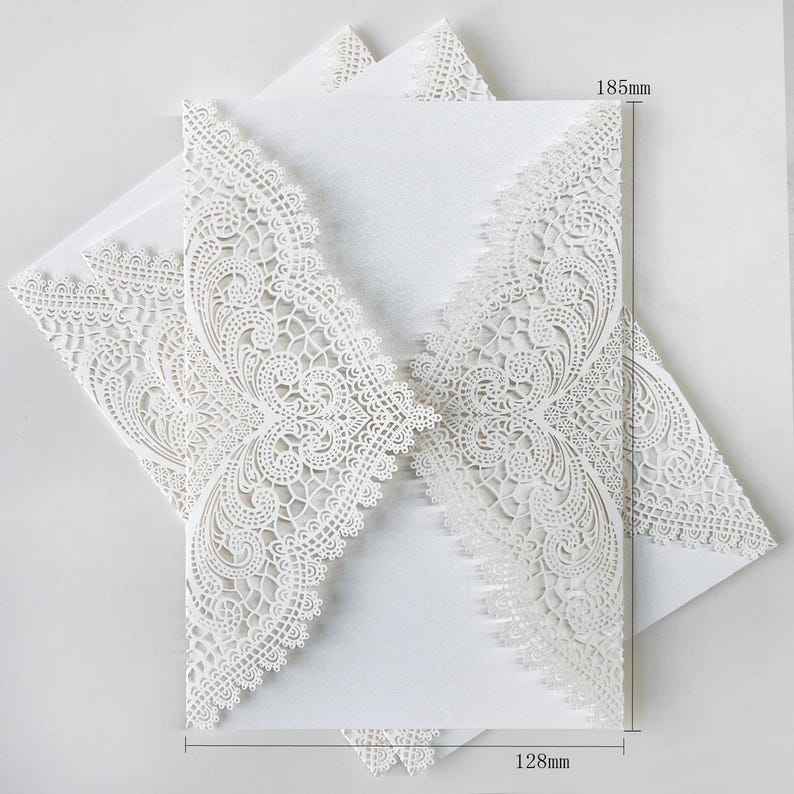 May include: White laser-cut wedding invitations with detailed floral lace patterns. The invitations measure 18.5cm high and 12.8cm wide. The paper has a textured finish, suitable for sophisticated occasions.