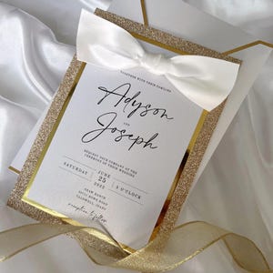 May include: A wedding invitation featuring the names "Adyson and Joseph" in elegant script. The invitation has a gold glitter border and a white satin bow. The details include the date, time, and location of the ceremony.