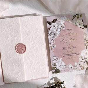 Op de afbeelding: Een trouwuitnodigingssuite met een bloemendesign in blush roze en wit. De uitnodiging bevat de namen "Cooper Cheng" en "Kary Char" met de datum "25 september 2022". De uitnodiging is verzegeld met een roze waszegel.