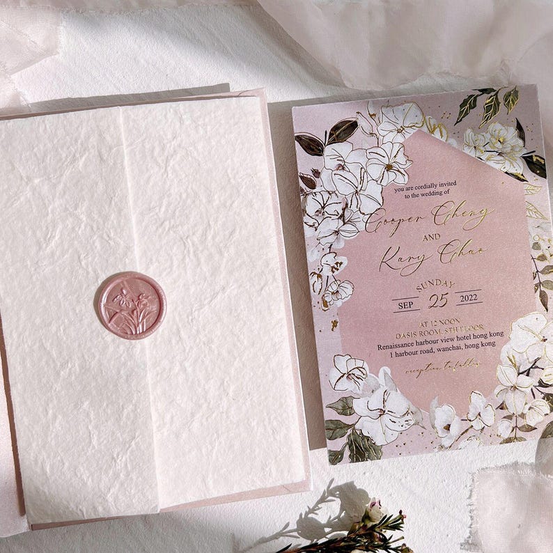 Op de afbeelding: Een trouwuitnodigingssuite met een bloemendesign in blush roze en wit. De uitnodiging bevat de namen "Cooper Cheng" en "Kary Char" met de datum "25 september 2022". De uitnodiging is verzegeld met een roze waszegel.