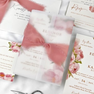 May include: Wedding invitation suite featuring floral designs and elegant calligraphy. The invitation is wrapped in translucent vellum and tied with a dusty rose ribbon. Other cards include RSVP and details cards. The suite includes the names Eleanor and Kara.