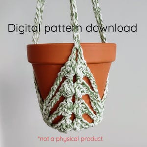May include: A crochet plant hanger with a white and green pattern, holding a terracotta pot. The text "Digital pattern download" is at the top of the image. The text "*not a physical product" is at the bottom of the image.