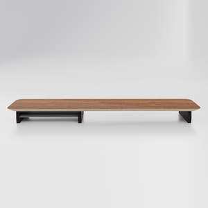May include: A wooden monitor stand with a shelf for storage. The stand is brown with a dark brown base.
