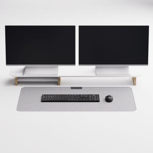 May include: A white desk with two black computer monitors on a white stand with wooden legs. A gray mouse pad with a black keyboard and mouse is on the desk.