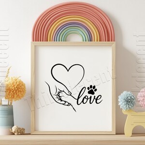 May include: A framed print featuring a black and white illustration of a hand holding a paw, forming a heart shape, with the word "love" below. A rainbow arch decorates the top, and a vase of flowers sits to the left.