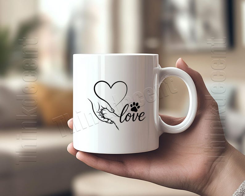 May include: White ceramic mug featuring a black graphic of a heart, a hand holding a paw, and the word "love." The mug has a curved handle and is held by a person. The design is simple and elegant, suitable for pet lovers.