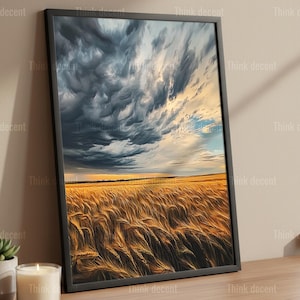 May include: Framed art print featuring a wheat field under a dramatic sky. The artwork displays a golden field of wheat beneath a sky filled with dark, swirling clouds. The print is in a black frame and rests on a wooden surface.