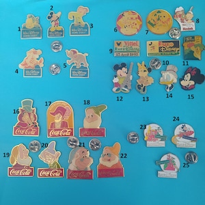 Op de afbeelding: Een verzameling van 25 vintage Disney- en Coca-Cola-speldjes. De speldjes tonen verschillende personages, logo's en ontwerpen. Sommige van de speldjes zijn van Euro Disney, waaronder een speldje met de tekst "Euro Disney Ouverture 13 Avril 92". Andere speldjes tonen Mickey Mouse, Donald Duck en andere Disney-personages. Er zijn ook verschillende Coca-Cola-speldjes, waaronder een speldje met de tekst "Coca-Cola" en een rood-wit ontwerp.