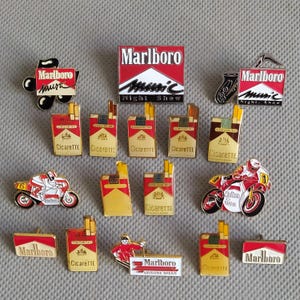 Może przedstawiać: Kolekcja metalowych emaliowanych przypinek z brandingiem Marlboro. Zestaw zawiera prostokątne znaki, kształty paczek papierosów z napisem Cigarette, wzory motocykli oraz logotypy muzyczne w kolorach czerwonym, białym, złotym i czarnym.