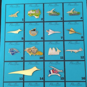 May include: A collection of sixteen pins on a blue background. The pins feature various designs, including airplanes, abstract shapes, and logos. The pins are in gold, silver, and various colors.