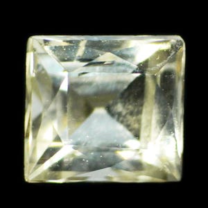 May include: A square-cut, translucent gemstone with a pale yellow hue and multifaceted surface. The stone features a clear, brilliant finish with sharp edges and a geometric design that reflects light across its polished, angular facets.