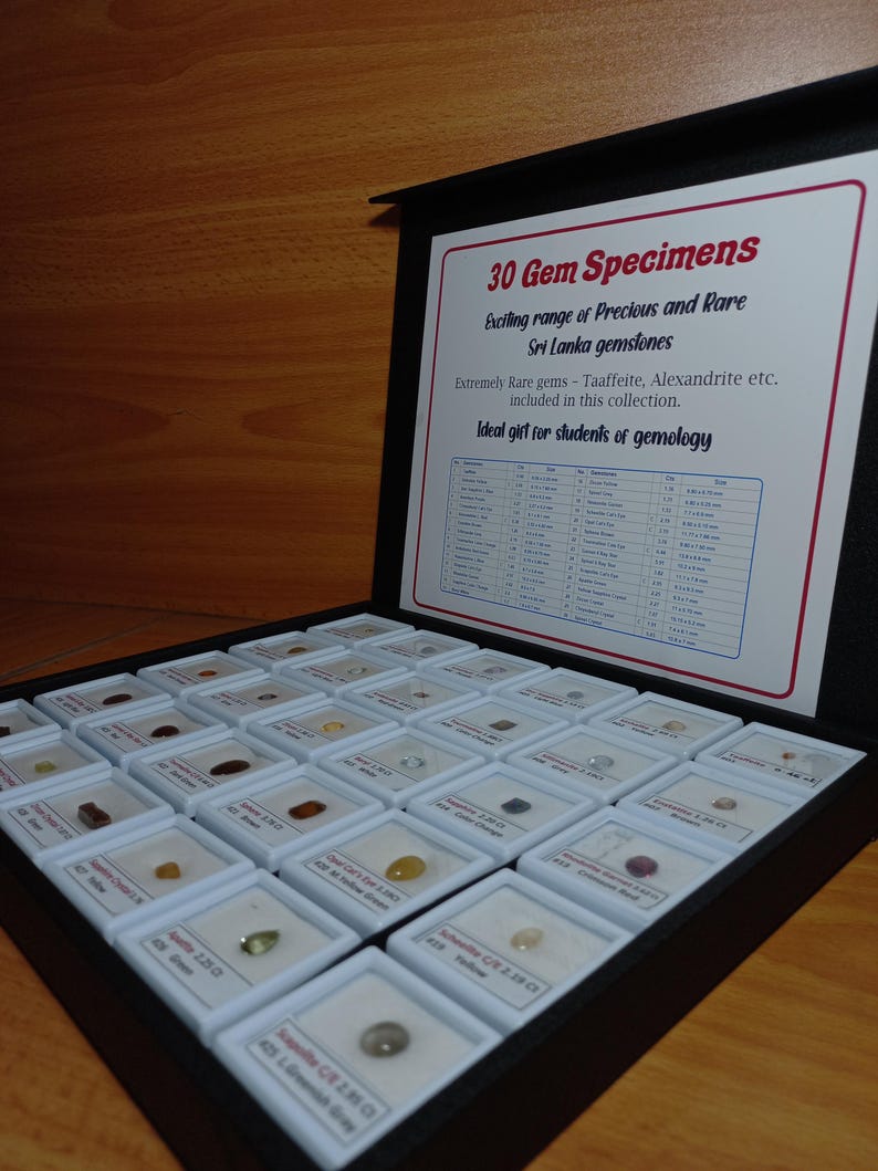 Może przedstawiać: Czarna gablota z 30 okazami kamieni szlachetnych, każdy w małym białym kwadracie. Gablota zawiera wydrukowaną kartę z tekstem "30 Gem Specimens" i "Exciting range of Precious and Rare Sri Lanka gemstones."