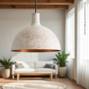 a modern living room with a large, white pendant lamp hanging from the ceiling, casting a warm glow over the space. The room is furnished with a white sofa and a wooden coffee table, creating a cozy and inviting atmosphere.