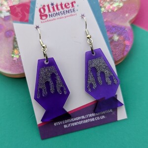 May include: Purple resin earrings with silver glitter and a dripping design. The earrings are on a white card with the text "glitter nonsense handmade resin jewellery" and the website address "etsy.com/shop/glitternonsense glitternonsense.co.uk".