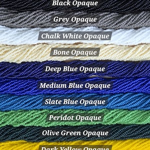 May include: Ten strands of small, round, opaque beads arranged horizontally in a color gradient. Colors include black, grey, chalk white, bone, deep blue, medium blue, slate blue, peridot green, olive green, and dark yellow, each labeled with text.